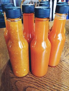 four bottles filled with orange sauce sitting on top of a wooden table