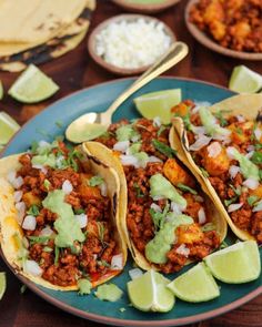 three tacos on a plate with lime wedges