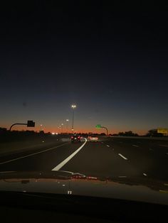 cars driving down the highway at night with street lights in the distance and traffic signs on either side