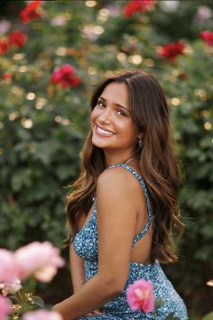 a beautiful young woman sitting on top of a pink rose bush smiling at the camera