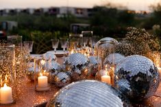 a table topped with lots of silver disco balls and lit candles next to each other