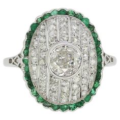 Here we have a fabulous emerald and diamond cluster ring crafted during pinnacle of the Art Deco movement. A single round faceted old European cut diamond sits slightly risen at the centre of the face in a full bezel setting. This principal stone proudly surmounts the concave backdrop consisting of 7 milgrain set channels filled with old cut diamonds which, in turn, are contained within an undulated border of perfectly matched emeralds around the outer edge. The piece is made complete by a ornate open under-gallery and split platinum band. Condition: Used (Very Good) Weight: 4.1 grams Ring Size: K (50) Face Dimensions: 18mm x 15mm Centre Diamond Weight: Approx. 0.50ct Diamond Details: Approx. Colour: G, Clarity: SI Total Remaining Diamond Weight: Approx. 0.55ct Total Emerald Dimensions: 32 Art Deco Emerald, Art Deco Movement, Ring Crafts, European Cut Diamonds, Diamond Cluster Ring, Diamond Cluster, Emerald Diamond, Cluster Ring, Diamond Gemstone