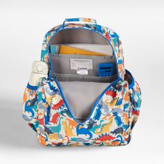 A backpack that's extra comfy and ready to handle the adventures of the day. Patterned with a colorful collection of dinosaurs stomping across the white exterior, the kids' large knapsack is constructed of supremely durable polyester made from recycled water bottles. A roomy interior holds everything your kid needs-books, school supplies, extra layers-and there's a padded pocket to keep their tablet protected. Outside pockets hold snacks, water bottles and more, and a strap secures a lunch box. Fun Travel Backpack With Zipper Closure, Playful White Backpack, Fun White Travel Backpack, Fun White Standard Backpack, White Backpack For Daycare, White Standard Backpack For Daycare, Back To School White Backpack, Books School, Bottle Picture