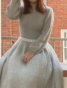 a woman in a gray dress is posing on a porch with her hat up and hands behind her head