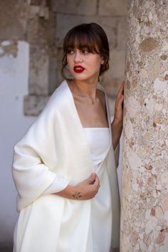 a woman in a white dress leaning against a stone pillar with her hands on her hips