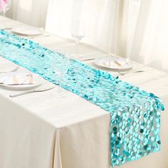 the table is set with white plates and blue sequins on it, along with silverware