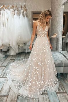 a woman in a wedding dress looking down at her gown hanging on the rack with other dresses behind her