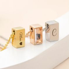 three personalized cube pendants on a gold chain, one with a photo and the other with a heart