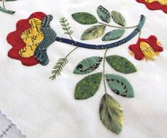 an embroidered table cloth with flowers and leaves on it