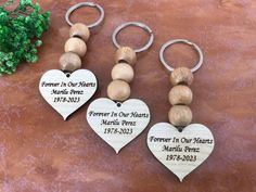 three wooden heart shaped keychains with names and date engraved on them, sitting next to a potted plant