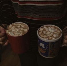 two cups of hot chocolate with marshmallows in them are being held by someone