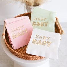 three baby napkins sitting on top of a white toilet next to a basket filled with flowers