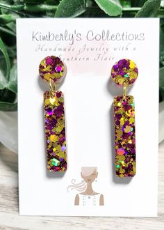 a pair of purple and yellow earrings on top of a card with a plant in the background