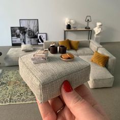 a hand holding a miniature model of a living room with couches and coffee tables