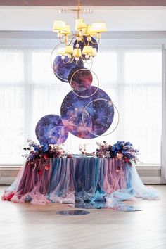 the table is covered with purple, blue and red cloths as it sits in front of a large chandelier