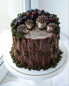 a cake decorated with pine cones, berries and hedgehogs on top of a tree stump