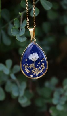 a blue and gold tear shaped pendant hangs from a chain with leaves in the background