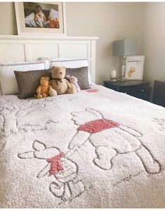 two teddy bears sitting on top of a bed with a white comforter and pillows