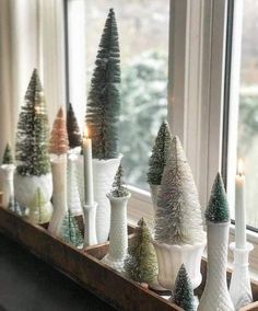 small christmas trees in white vases on a window sill with candles and other decorations