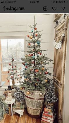 a small christmas tree is in a bucket on the floor next to a window and bookshelf