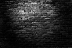 a black and white photo of a brick wall with light coming through the hole in it