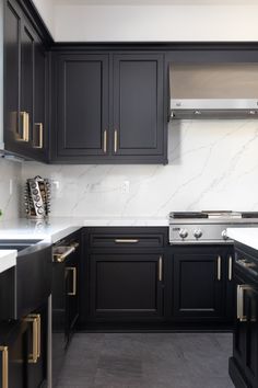 a kitchen with black cabinets and white marble counter tops, along with stainless steel appliances