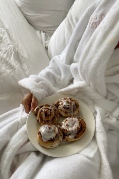 a person laying in bed holding a plate with food on it and wrapped in blankets