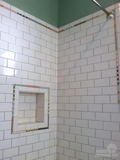 a white tiled shower with a square window in the middle and green walls behind it