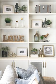 a living room filled with lots of white bookshelves covered in pictures and plants