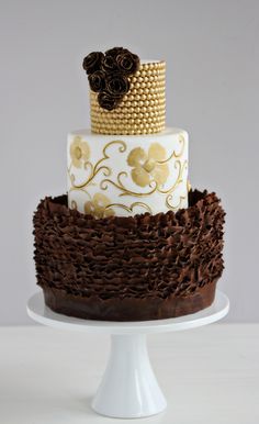 a three tiered cake with brown and gold decorations on it's top layer