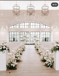 the aisle is decorated with white flowers and greenery for an elegant wedding ceremony in front of large windows