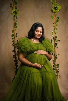 a pregnant woman in a green dress standing on a swing with greenery around her