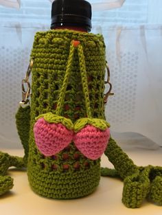 a green crocheted water bottle holder with pink handles and two ears on it