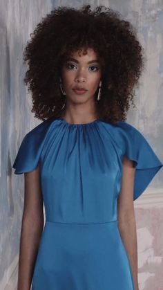 a woman in a blue dress with an afro standing next to a wall and looking at the camera