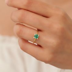 a woman's hand holding a ring with a green stone on the middle finger