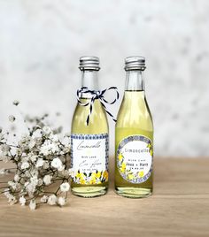 two bottles of lemonade sitting on top of a table next to some white flowers