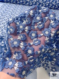 a woman's hand is holding a blue and white lace fabric with flowers on it