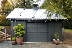 two potted plants sit in front of a garage with a metal roof and chimney