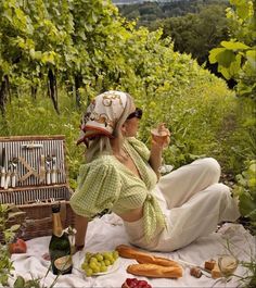 a woman sitting on the ground with food and wine