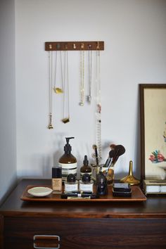 a wooden dresser topped with lots of personal care items next to a framed painting on the wall