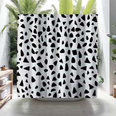 a shower curtain with black and white spots on it in a bathroom next to a potted plant