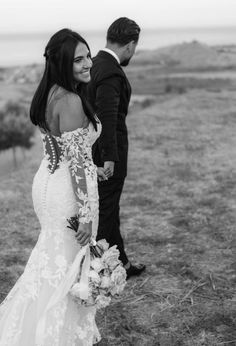 a bride and groom walking in the grass near each other with their back to the camera