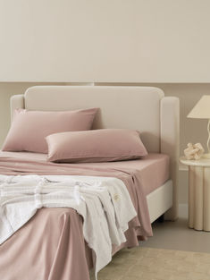 a bed with pink sheets and pillows on top of it next to a night stand