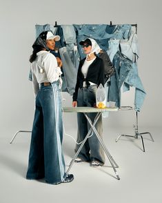 two women standing in front of a clothes rack and ironing board with jeans on it