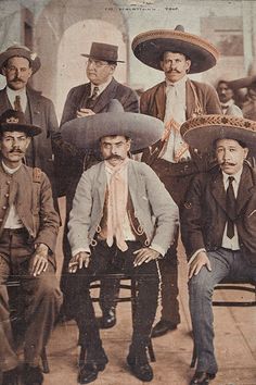 a group of men sitting next to each other in front of a white building with sombreros on their heads