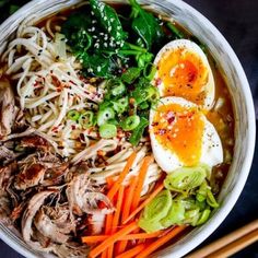 a bowl filled with noodles, meat and vegetables next to chopsticks on a table