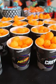 several cups filled with food sitting on top of a black table covered in orange candies