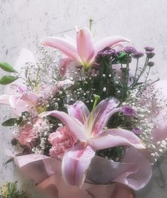 a bouquet of pink lilies and baby's breath in front of a white wall