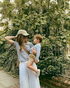 a woman holding a small child in her arms while standing next to a lush green tree