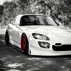 a white sports car with red rims parked on the side of the road in front of some trees